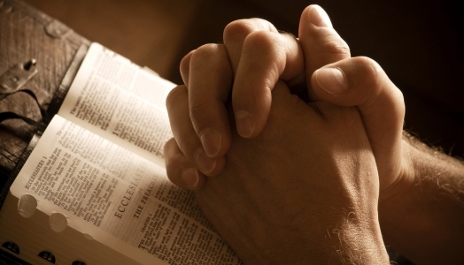 Hands folded in prayer on an open Bible